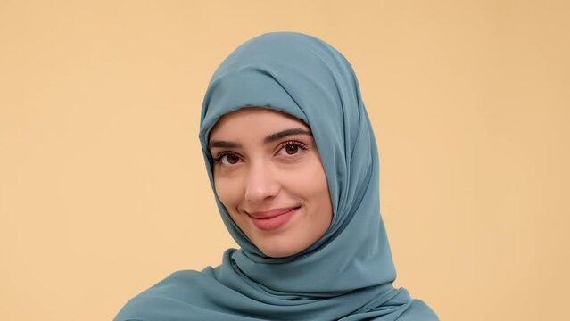 Portrait of a shy young smiling Muslim woman looking at camera on beige background. Shy emotion with happiness and joy. Adorable, bashful arabian woman.