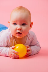 Portrait of a baby girl on a pink background with a yellow ball