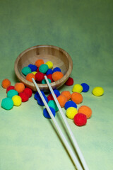 vertical photo of a wooden bowl and chopsticks for eating with colored balls for practice and selection