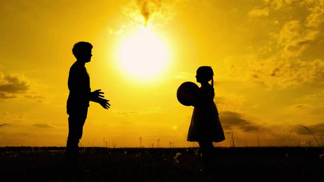 Children playing with ball in park at sunset. Happy boy, girl are playing throwing ball to each other. Happy family. Children have fun with ball in park in sun. Children team, dreams. Kids Silhouette