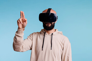 Young man in vr helmet making tap gesture with two fingers while exploring metaverse. Person in headset enjoying simulation activity and playing virtual reality games in cyberspace