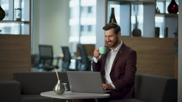 Smiling business man working office looking laptop screen. Manager drinking tea