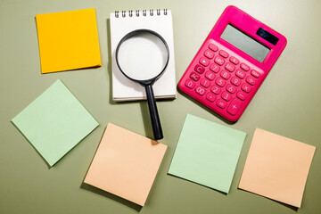 Closeup view of magnifying glass and calculator with an empty notebook and note paper