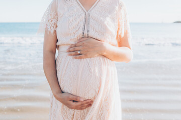 close up cropped photo of pregnant mother mom in pink maternity lace dress with both hands holding...
