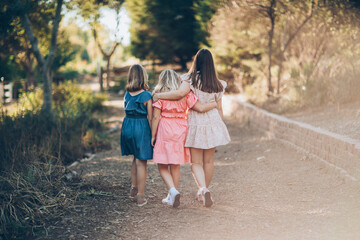 Three girls walking away from the camera with their arms around each other down a wooded path