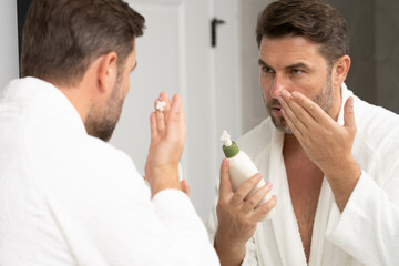 Young happy manful guy applying face cream. Close up shot of attractive man with healthy skin,...