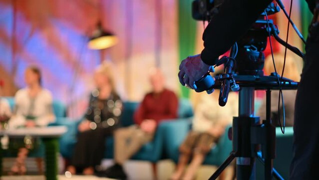 Cameraman spinning focus wheel on a professional camera while filming a television talk show. Video production backstage in a dark studio