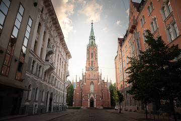 Fototapeta premium Panorama of the Saint Gertrude old church by a pedestrian cobblestone street of Riga at dusk in Summer. also called veca svetas gertrudes evangeliski luteriska baznica, it's a gothic lutheran church.