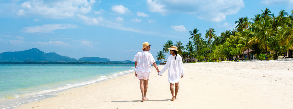 Koh Mook a young couple of caucasian men and Thai Asian woman walking at the beach in Thailand