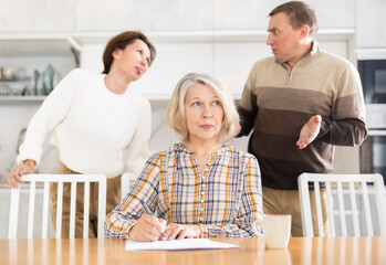 Competitive middle-aged man and woman conflicting and old woman writing inheritance sitting at...
