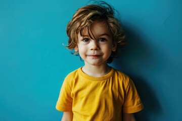 Confident boy in yellow shirt standing by blue wall.