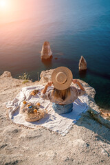 Fototapeta na wymiar woman sea travel. photo of a beautiful woman with long blond hair in a pink shirt and denim shorts and a hat having a picnic on a hill overlooking the sea