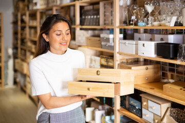 Smiling woman consumer choosing wooden box in furniture shop