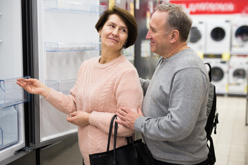 Fototapeta na wymiar Middle aged wife and husband picking new refrigerator in shop of household appliances.