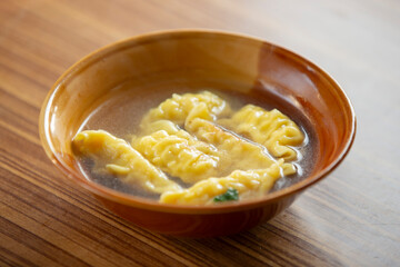 Chinese dumpling soup in a bowl on a wooden table.