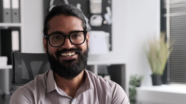 Close up portrait of happy and satisfied Indian male CEO in office, looking and smiling at camera. Joyful manager, relaxed office worker, positive businessman.
