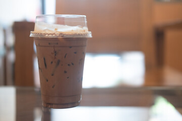 Iced coffee Mocha in plastic mugs on the coffee shop table with the background of light shining through the door.