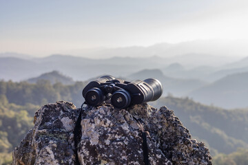 binoculars on top of rock mountain at beautiful sunset background.
