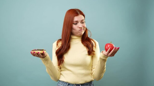 Woman choosing between eating healthy or not, holding an apple in one hand and a donut in the other