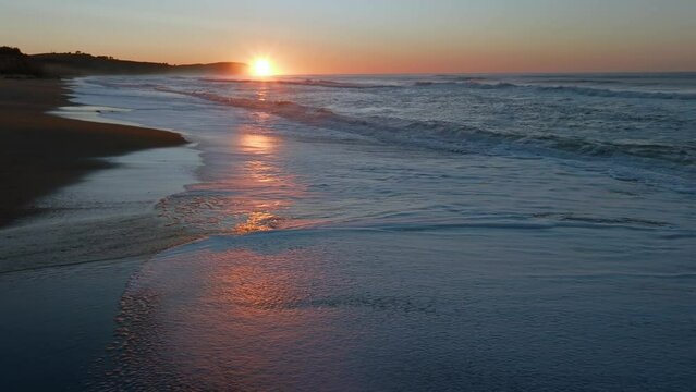 Aerial: Ocean beach surf and beach in sunrise. Oamaru, Otago, New Zealand.