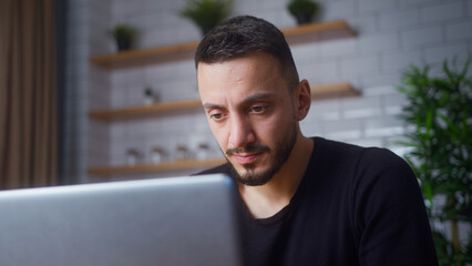 adult man sit in kitchen using laptop watching video, surfing internet, using social media, chatting with friends. Medium close-up