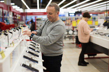 Fototapeta na wymiar Caucasian aged man choosing digital wristwatches in electronic store.