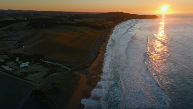 Aerial: Ocean beach surf beach and farmland in sunrise. Oamaru, Otago, New Zealand.