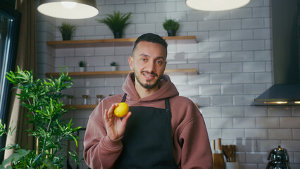 Vlogger man in an apron standing in kitchen talking to camera, recording video about making lemonade at home. Online broadcast, man leads food blog or course