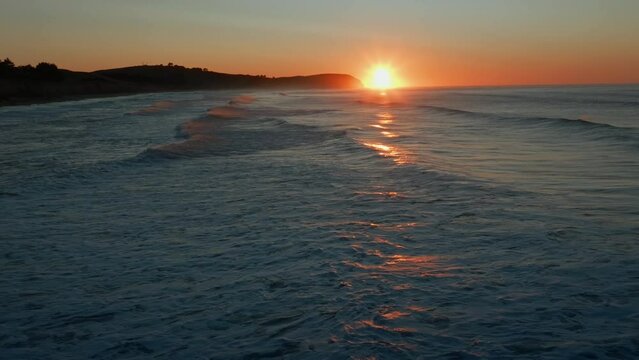 Aerial: Ocean beach surf and beach in sunrise. Oamaru, Otago, New Zealand.