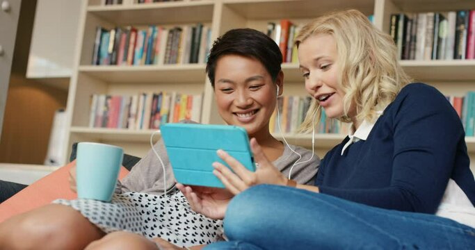 Women friends, tablet and video call on sofa with smile, talking or wave hello to contact with earphones. People, girl and digital touchscreen with web chat, communication and happy with social media