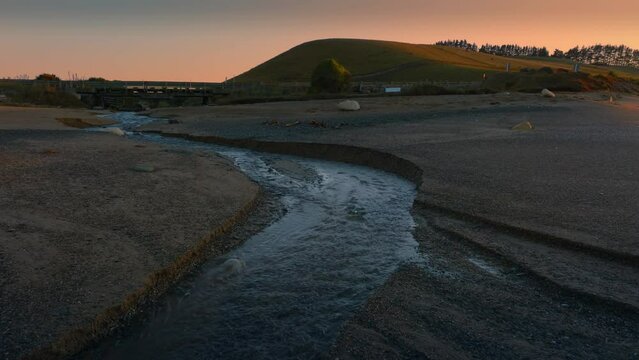 Aerial: Ocean beach surf and river in sunrise. Oamaru, Otago, New Zealand.