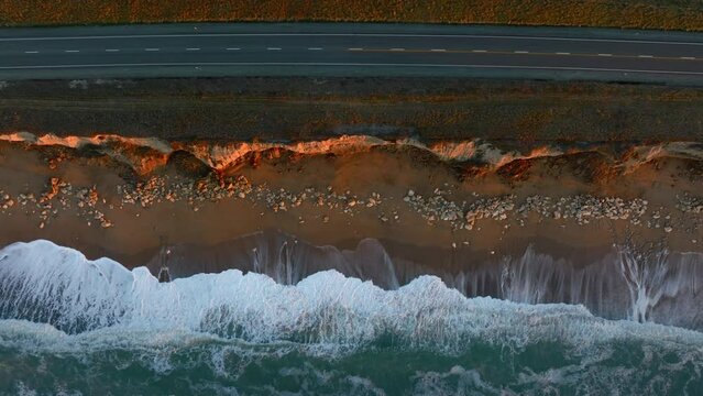 Aerial: Ocean beach surf, country road and  farmland in sunrise. Oamaru, Otago, New Zealand.