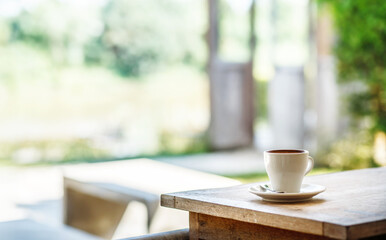 White coffee cup on wooden table with nature background and sunlight in park