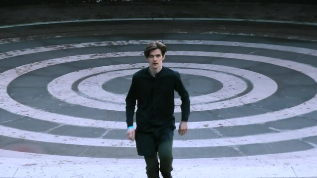 Young man dressed in black running up the stairs of stone amphitheater. Stock clip. Asphalt painted in white and black rings.
