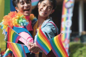 Two gay men join in the fun at the Pride parade, showing and waving flags in celebration of Pride...