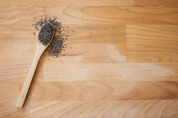 Black chia seeds on a wooden spoon on a wooden board with negative space