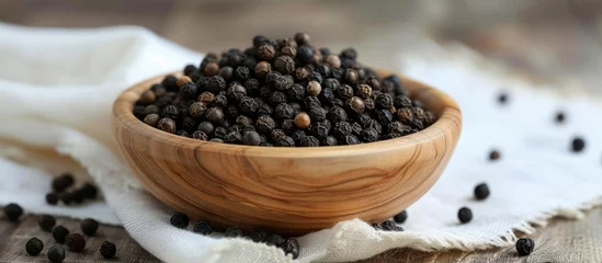  Numerous black peppercorns rested in a wooden bowl on a white cloth. © 2rogan