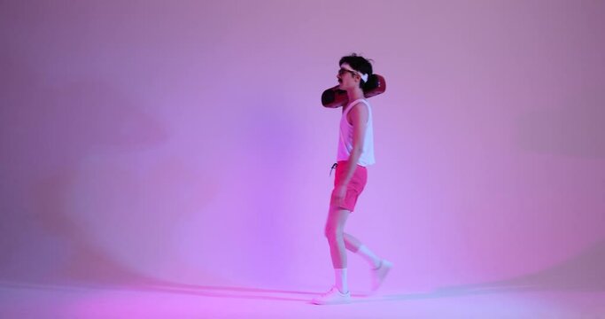 Friendly, freaky Caucasian 90s man enters frame with ghettoblaster on shoulder, listening music and dancing, standing over purple background.