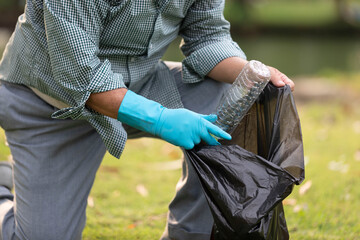 close up volunteer hands picking up plastic bottle and putting garbage bag in the park