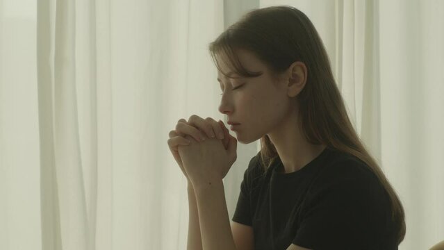 Woman Praying with Hands Clasped &ndash; Peaceful Moment of Spiritual Reflection Indoors
