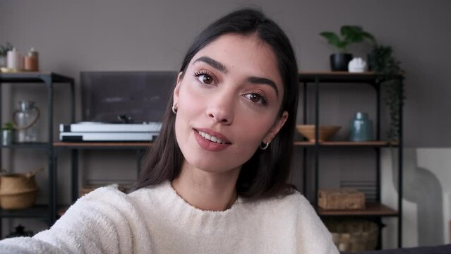 Friendly Caucasian woman vlogging at home, talking to camera. Broadcasting in social media, greeting by waving hand, looking at camera, holding phone.
