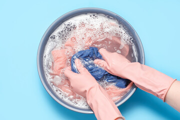 Female hands in rubber gloves washing clothes in basin on blue background, top view.