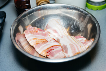 Raw Sliced Bacon Ready for Cooking. Uncooked slices of bacon arranged in a stainless steel bowl on...