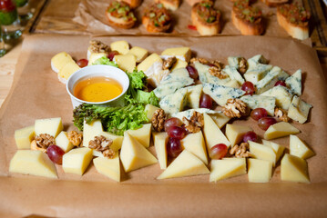 Artisan Cheese Platter with Grapes, Nuts, and Honey. An appetizing cheese platter featuring a variety of gourmet cheeses, accompanied by fresh grapes, walnuts, and a bowl of honey.