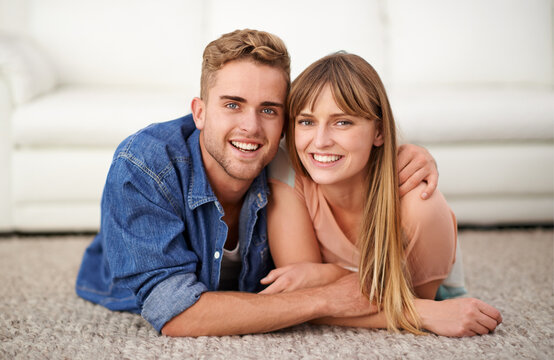 Happy, portrait and couple lay on carpet of living room in house to relax, bonding and romance for love. Man, woman and together on rug in lounge of home with affection, care and hug for connection