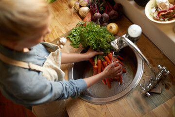 Person, sink and cleaning carrot in kitchen, health and hygiene with cooking food and top view....