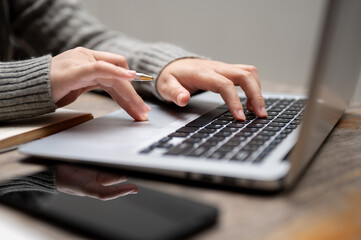 Close-up image of a woman typing on a keyboard, working on her laptop computer at a table.