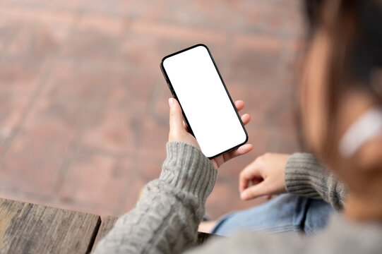 A close-up image of an Asian woman using her smartphone while sitting outdoors.