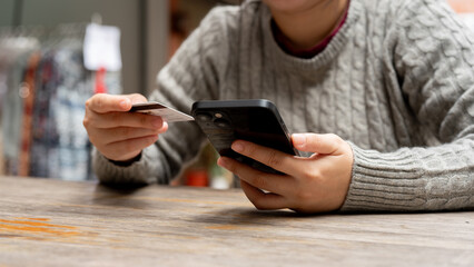 A cropped shot of a woman holding her smartphone and a credit card while sitting at a table.