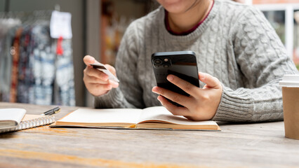 A cropped shot of a woman holding her smartphone and a credit card while sitting at a table.